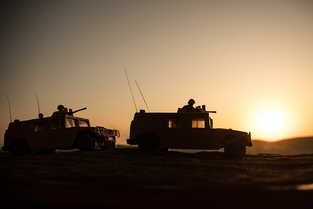 Silhouettes of two military tanks and soldiers against a setting sun.