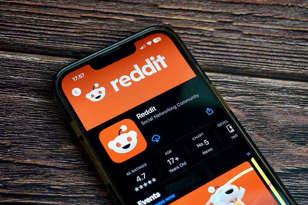Smart phone screen with orange logo of Reddit app displayed.