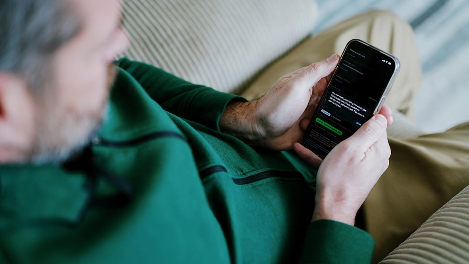 An elderly man looks down at his smartphone, which displays a block of text.