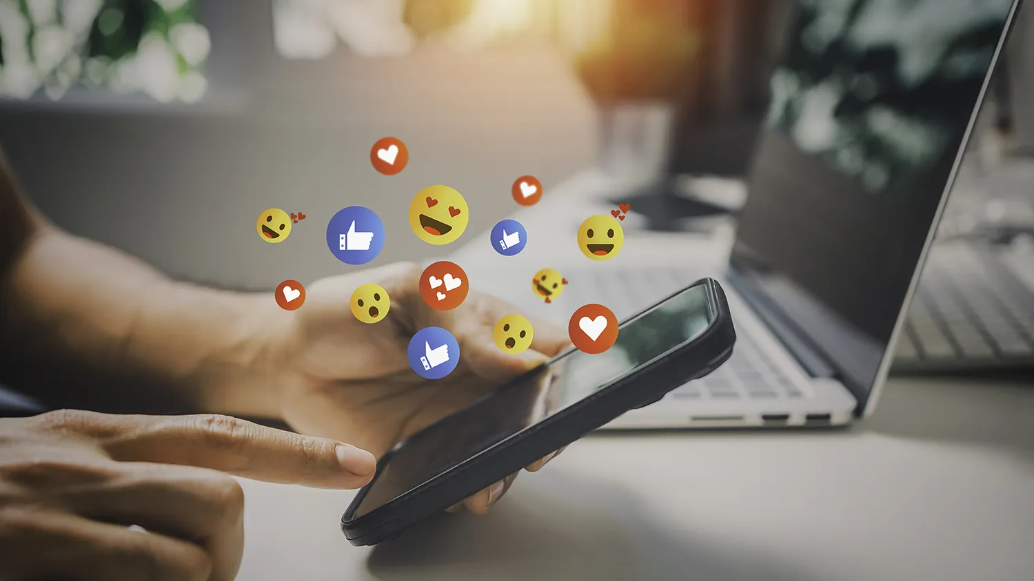 A person scrolls on a smartphone with a cloud of emojis and "like" symbols around it