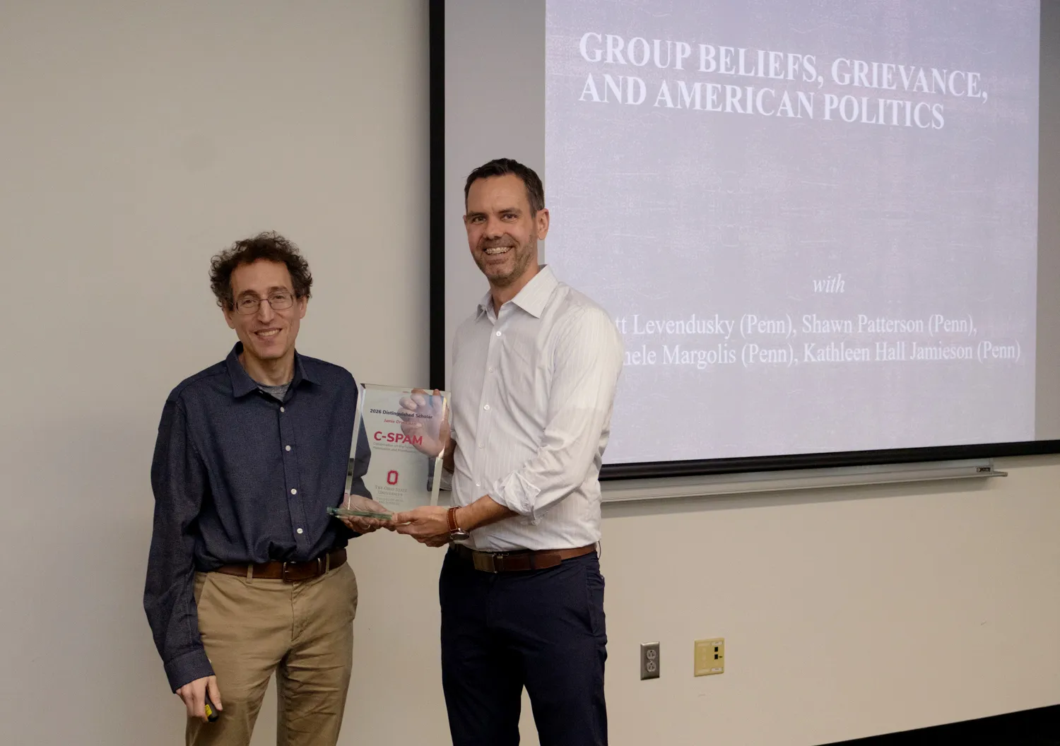 Kurt Gray and Jamie Druckman holding glass trophy with the words "2026 C-SPAM Distinguished Scholar"